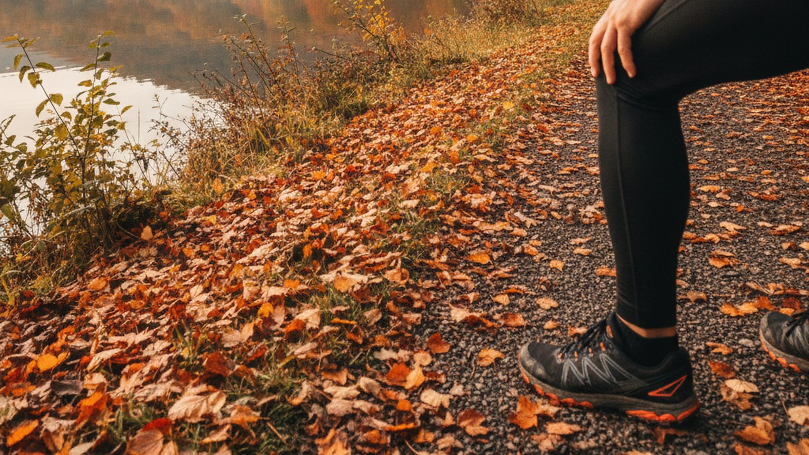 Runner pausing on an autumn lakeside path with a hand on the front of the knee